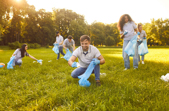Portrait of a happy smiling young people volunteers in gloves with trash bag collecting plastic garbage in the summer park. Environmental pollution, volunteering and ecology concept.