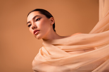 Beautiful portrait of a young brunette woman gracefully draped in beige fabric against a soft...