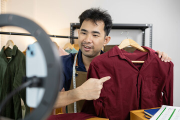 A man is live streaming his shirt on his mobile phone. On the table are boxes and shipping...