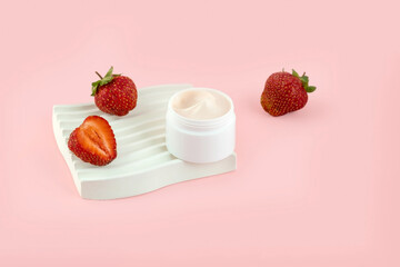 close-up of collagen cream in an open glass jar and strawberries on a plaster tray on a pink background