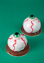 Mousse cakes in the shape of eyes for Halloween party on green background
