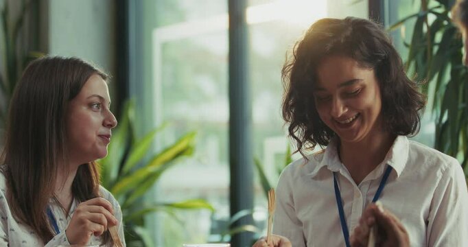 Three caucasian intern teammates enjoy lunch together in slow motion at bright sunny office cafeteria