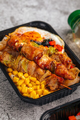 Grilled chicken skewers with corn noodles and fried egg in takeout container