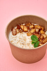 Cinnamon apple oatmeal in brown cup with mint on pink surface for breakfast delight