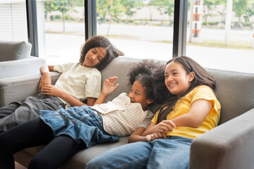 Happy Diverse Teen Girls Relaxing on Sofa by Window, Three Smiling Young Friends Lounging Together...
