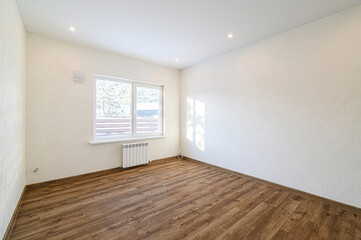 bright, empty room with wooden flooring, textured white walls, a window showing a winter scene, and...