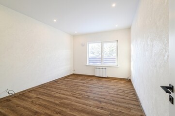 Bright, empty room with wood flooring, textured white walls, a window showing a winter scene, and recessed lighting