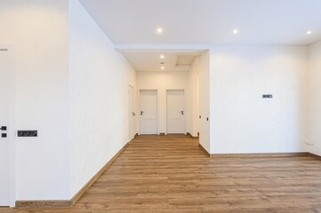 Bright interior shot of a hallway with white walls, wooden floors, and multiple white doors....