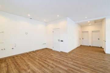bright, spacious room with wooden floors and white walls. Three white doors are visible. Some...