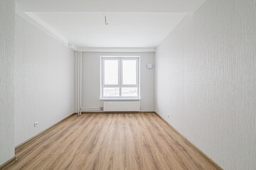 empty, bright room with light walls, wood-look laminate flooring, a window centered on the far...