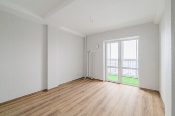 bright, empty room with wood floors and white walls. A balcony is visible through the window