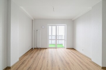 bright, empty room with wood floors and white walls. A balcony is visible through the window