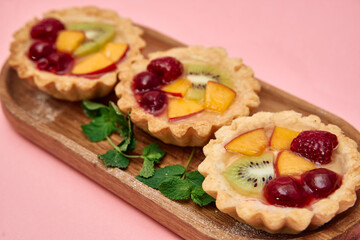 Delicious fruit tarts with kiwi, peach, raspberry, and cherry on wooden tray with mint leaves