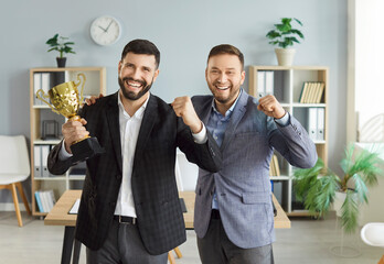 Portrait of a happy smiling young company employees looking cheerful at camera holding prize cup...