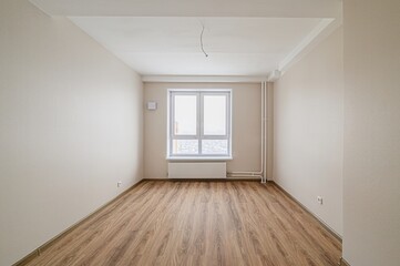 bright, empty room with wood flooring, light beige walls, and a large white window. A radiator sits under the window