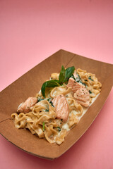 Creamy salmon fettuccine with spinach garnished with fresh basil in a brown paper bowl