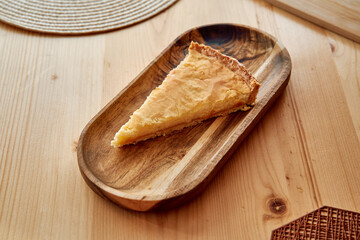 Lemon tart slice on wooden plate in sunlit setting on wooden table
