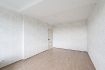 empty room with light-colored walls and laminate flooring. A door is visible on one wall. The room...