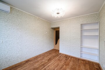 bright, empty room featuring floral wallpaper, wood flooring, and a crystal chandelier. A built-in...