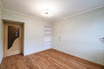 Empty room with patterned wallpaper, wood-look floor, a wooden door with decorative glass, and a...