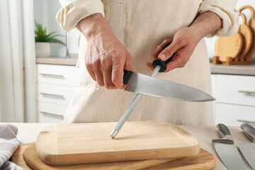 Man sharpening knife with sharpener at beige table indoors, closeup
