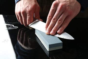 Man sharpening knife with sharpener at mirror table, closeup