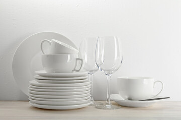 Different clean dishware on light wooden table near white wall