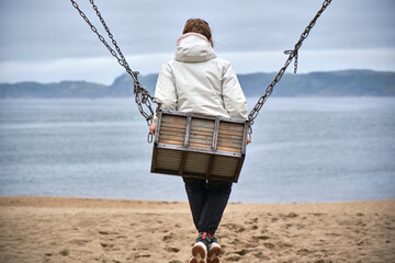 girl on a swing against the backdrop of the sea and mountains