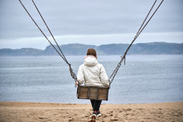 girl on a swing against the backdrop of the sea and mountains