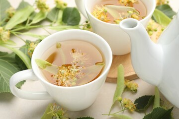 Fresh linden tea in cups, teapot and flowers on white table, closeup
