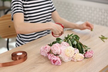 Florist making bouquet of peonies at wooden table in flower shop, closeup