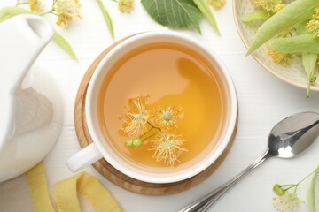 Fresh linden tea in cup and flowers on white wooden table, flat lay