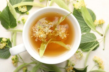 Fresh linden tea in cup and flowers on white table, flat lay