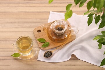 Tasty green tea in glass cup, teapot, brew and leaves on wooden table, above view