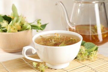 Fresh linden tea in cup, teapot and flowers on white table, closeup