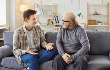 Adult son and a senior father talking. Old man in his 60s sitting on the couch together with his...
