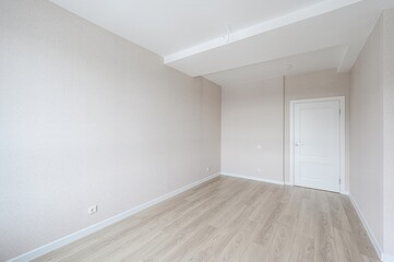 bright, empty room features light wood flooring, neutral walls, a white door, and a clean,...