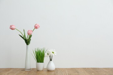 Beautiful flowers in vases and other floral decor on wooden table near white wall indoors, space for text