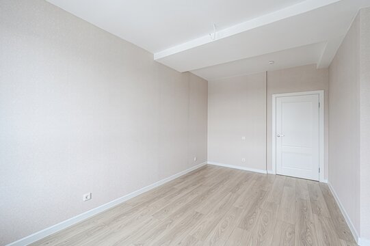 Fototapeta bright, empty room features light wood flooring, neutral walls, a white door, and a clean, minimalist aesthetic