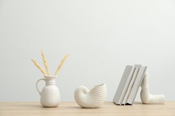 Different decor and books on wooden table near white wall indoors