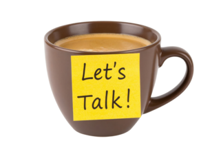 A brown coffee cup filled with coffee has a yellow sticky note on it that says "Let's Talk!".