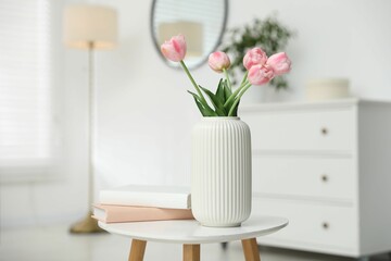 Beautiful tulip flowers in vase and books on white table indoors