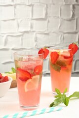 Refreshing drink with strawberries, mint and ice on white table against grey textured background, closeup