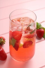 Refreshing drink with strawberries and ice on pink wooden table, closeup