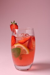 Refreshing drink with strawberries, mint, lemon and ice in glass on pink background, closeup