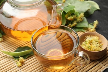 Tasty linden tea in cup, teapot, leaves and flowers on dark table, closeup