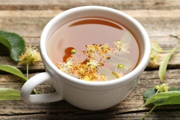 Tasty linden tea in cup, leaves and flowers on wooden table, closeup