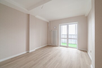 empty room with light walls and wood flooring is bathed in natural light from a balcony door. The...