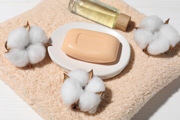 Soap bar, cotton flowers, cosmetic product and towel on white wooden table, above view