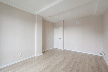bright, empty room with light wood flooring, beige walls, a white door, and white trim